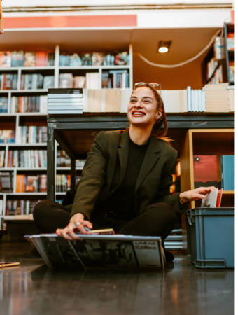 Portrait of smiling young brunette holding several vinyls while sitting on the floor at store. LPs gives whole different dimension to the music.