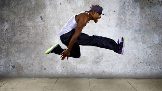 Black urban hip hop dancer jumping high on a concrete background