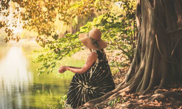 A young woman is sitting under a tree by the river