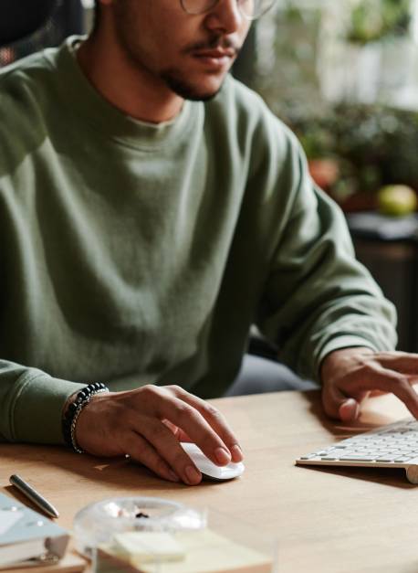 Young man in casualwear clicking mouse and pressing key of computer keyboard while working over new software by workplace