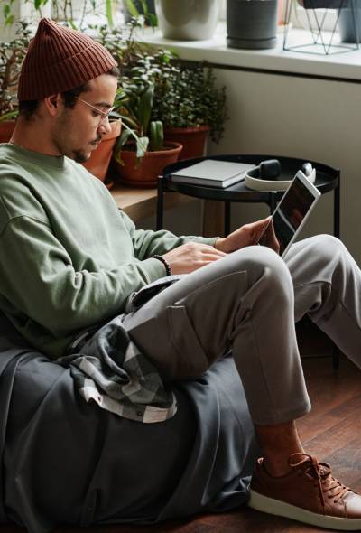 Young serious webdesigner with laptop concentrating on network while sitting in comfortable armchair in office with many green plants