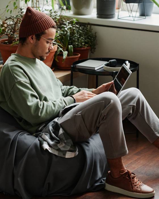 Young serious webdesigner with laptop concentrating on network while sitting in comfortable armchair in office with many green plants