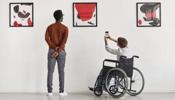 Back view portrait of young woman using wheelchair taking photo of artwork while visiting accessible museum, copy space